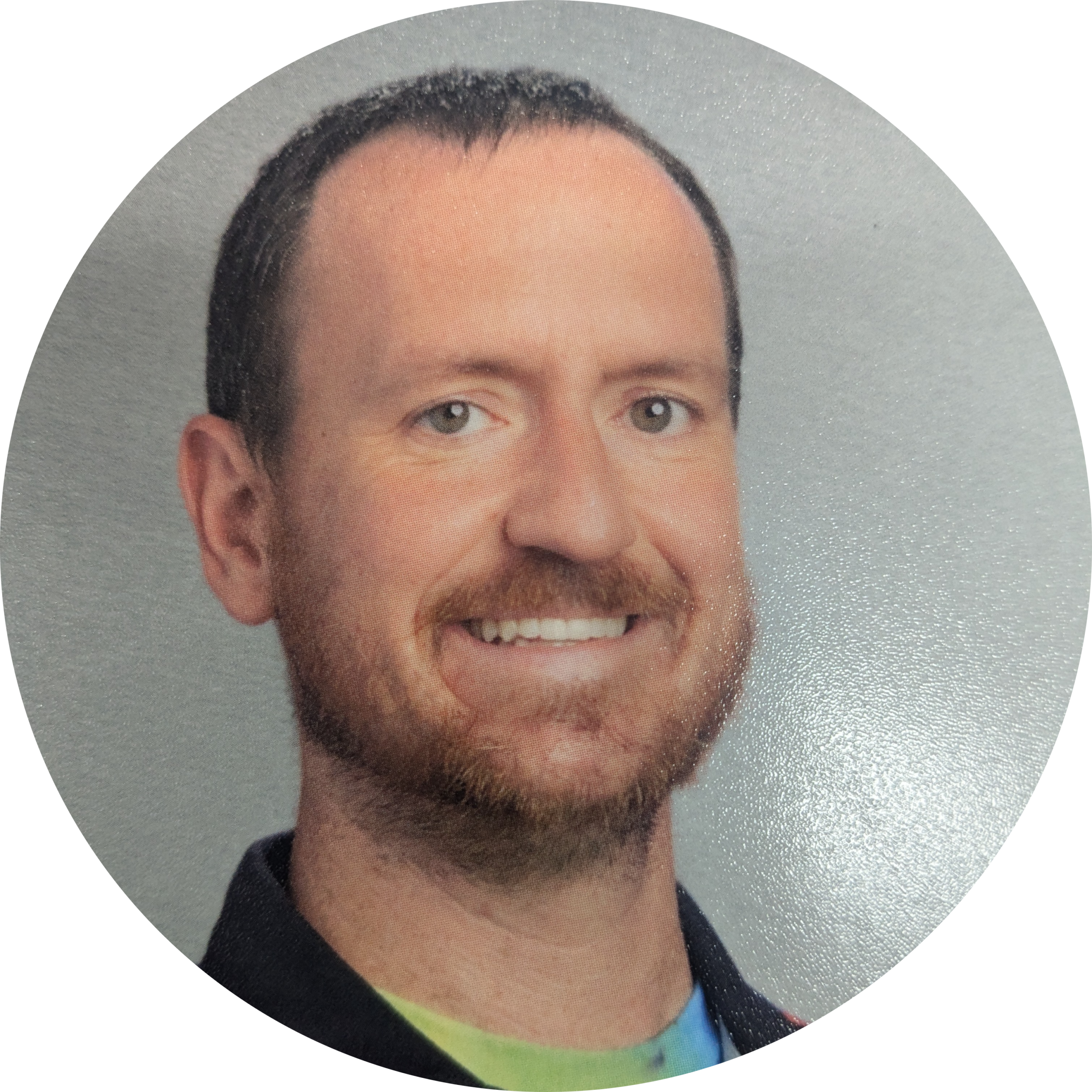 Head-and-shoulders portrait of a smiling man with short dark hair and light beard against a gray backdrop